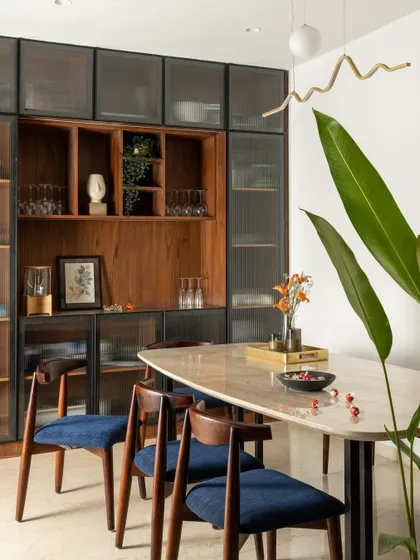 The dining area, where a marble-top table and navy blue chairs are set against the stunning backdrop of the custom-built crockery unit.