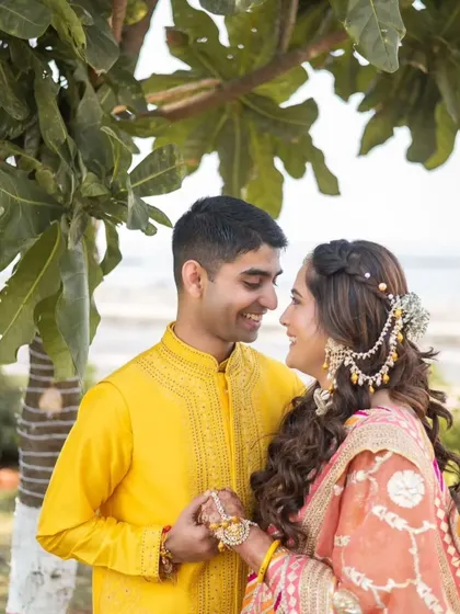 A romantic shot of the couple. The bride's hair is styled in a beautiful half-up braid, adorned with a passamer, a perfect Haldi hairstyle.