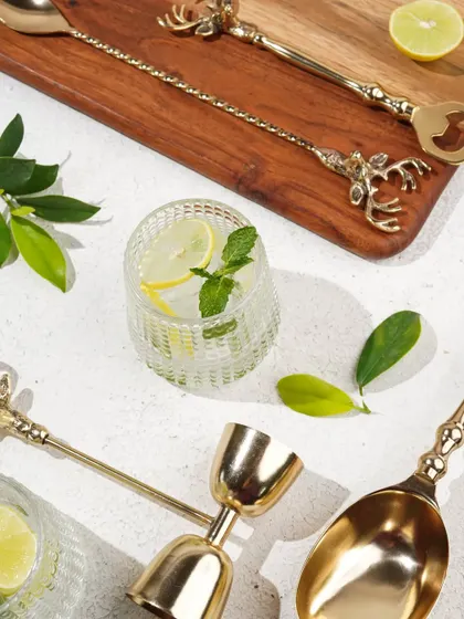 A top-down view of the classic brass barware set, styled with hard light to create dramatic shadows and highlight the golden finish.