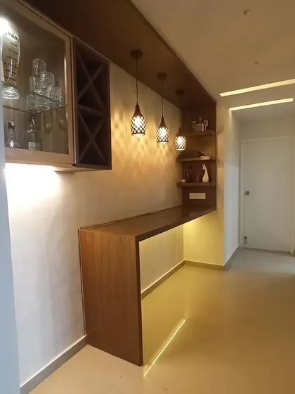 A compact bar unit designed for a passage area. It features a sleek wooden countertop, open shelving, and overhead cabinets with a wine rack, all illuminated by stylish pendant lights.