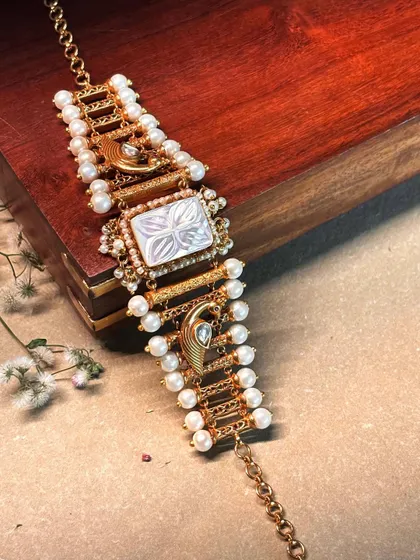 A delicate and unique bracelet featuring a carved mother-of-pearl center and peacock motifs, lined with pearls.