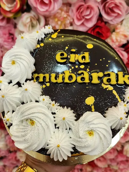 A rich chocolate "Eid Mubarak" cake, decorated with white frosting rosettes and a sprinkle of gold dust for a festive touch.