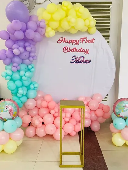 A pastel-colored unicorn-themed first birthday party. The setup includes a half-moon balloon arch on a circular backdrop and unicorn foil balloons.