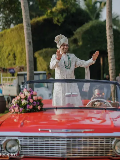 The groom arrives in style, making a grand entrance in a classic red convertible for his destination wedding baraat.
