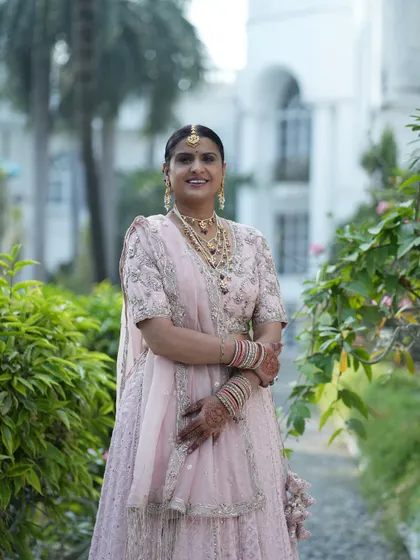 A full-length shot of a beautiful mother of the bride in a pastel pink lehenga. The makeup is soft and glamorous, designed to make her feel special and confident.