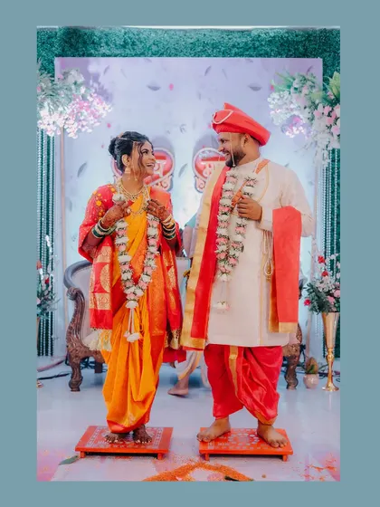 A full-length portrait of the couple during their 'Jaimala' ceremony, standing on small stools as is traditional.