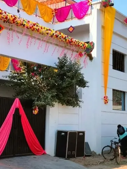 A house entrance decorated with a floral garland, hanging strings, and a pink drape over the gate.