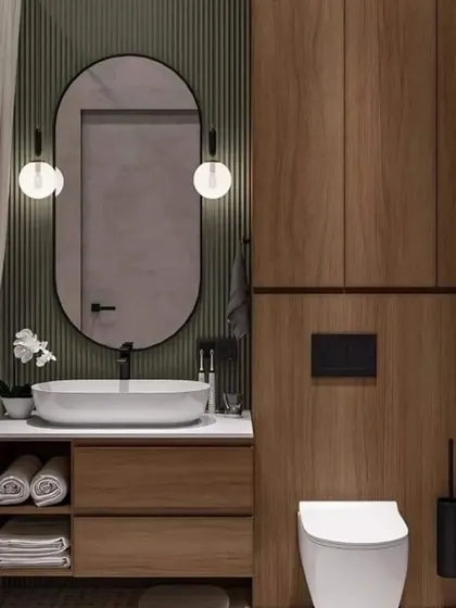 A cozy and modern bathroom with dark wood panelling and a simple oval mirror. The wall-mounted sconces provide soft, flattering light.