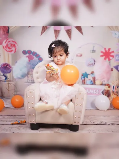Welcome to Candy Land. This little girl is sitting in a miniature armchair in a set decorated with lollipops, ice cream cones, and a ferris wheel, creating a sweet and colorful birthday theme.