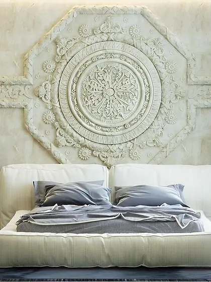 This bedroom features a stunning, large-scale carved mandala as a headboard, adding a touch of traditional Indian artistry to a modern space. The low bed and minimalist side tables keep the focus on the intricate wall detail.