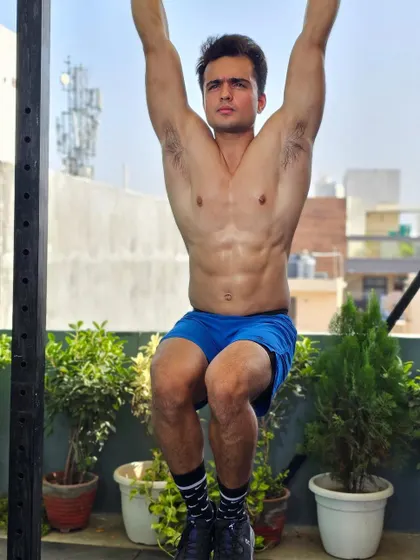 A raw, unedited shot from a photoshoot, holding a hanging leg raise. Core strength is the centerpiece of all functional movement.