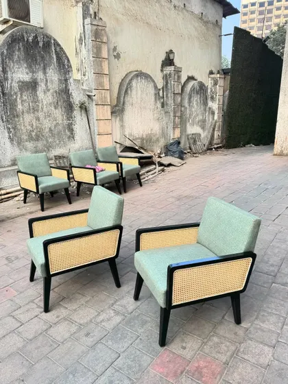 A closer look at a pair of the sage green lounge chairs, showing the contrast between the black frame and the light cane.