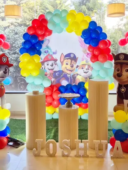 A bright and cheerful Paw Patrol birthday setup with a rainbow-colored balloon arch and character standees.