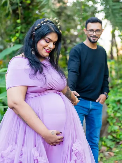 A portrait focusing on the mother-to-be, cradling her bump. The soft purple gown and the lush green background create a gentle and feminine look for this outdoor maternity photo.