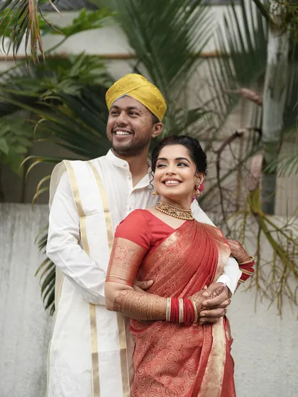 A happy couple shot. The bride's airbrushed makeup looks radiant and natural, perfectly complementing her red saree and her joyful smile.