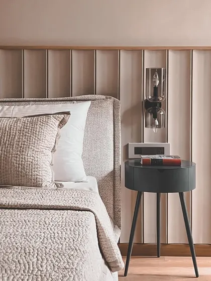 This bedroom design features a fluted back panel behind the bed, adding texture and rhythm to the space. The simple, three-legged side table is a modern touch that complements the clean lines.
