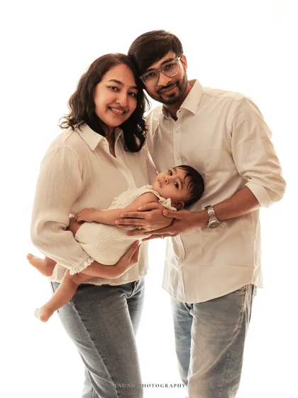 A classic family pose with parents holding their baby. The clean white background keeps the focus on their connection.