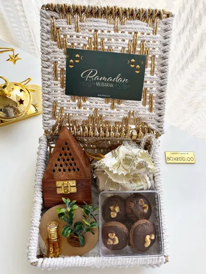 This Ramadan hamper in a woven basket includes a wooden Bakhoor burner, Attar, and chocolate-covered dates.