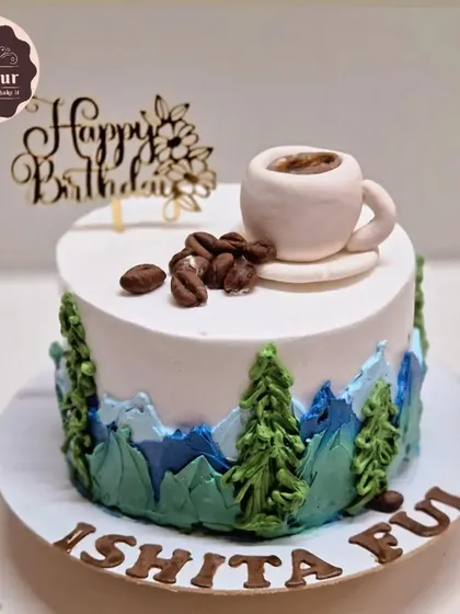 A mocha-flavored cake for someone who loves both coffee and mountains. The design features a piped mountain range and a tiny, edible coffee cup on top.