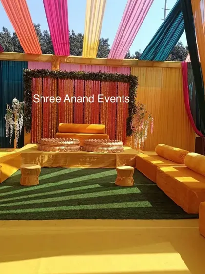 The main seating stage for a Haldi ceremony, with a backdrop of marigold strings and bright, colorful drapes.
