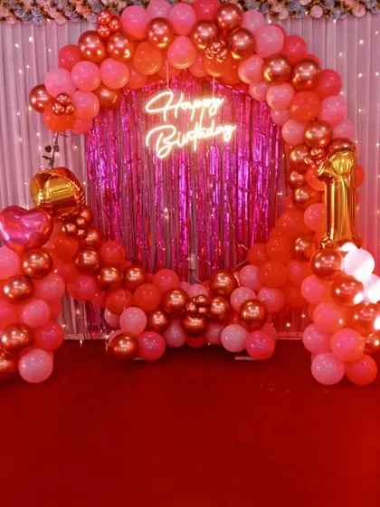 A vibrant pink and rose gold balloon arch against a shimmer backdrop for a first birthday.