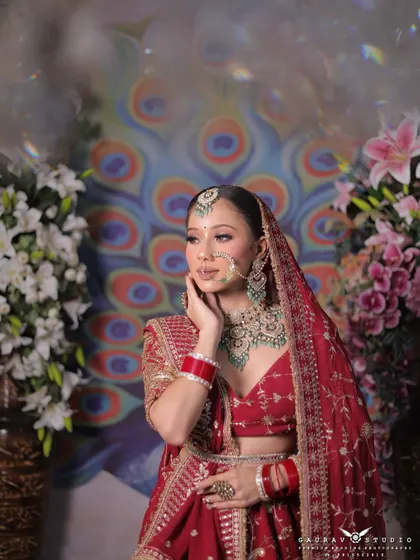 Capturing a moment of quiet grace, this photo shows the bride in her red lehenga, gently touching her face. The lighting enhances the sparkle of her green and white jewellery.