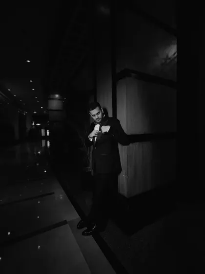 A dapper groom, captured in a moody, low-light portrait. This black and white shot has a classic, cinematic feel.
