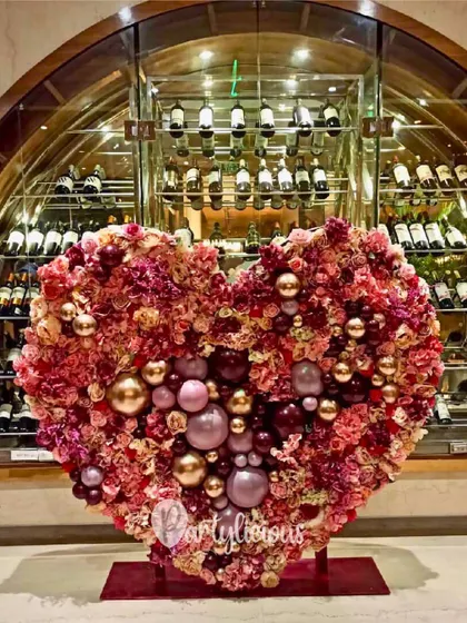 A magnificent heart-shaped installation made of flowers and balloons, set against a wine cellar backdrop, perfect for a romantic celebration or wedding event.
