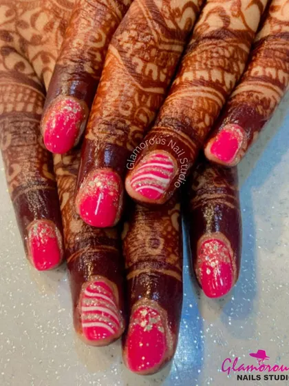 For the bride who loves a pop of color. This set features bright pink nails with silver glitter accents and intricate white swirl patterns, designed to stand out alongside traditional mehendi.