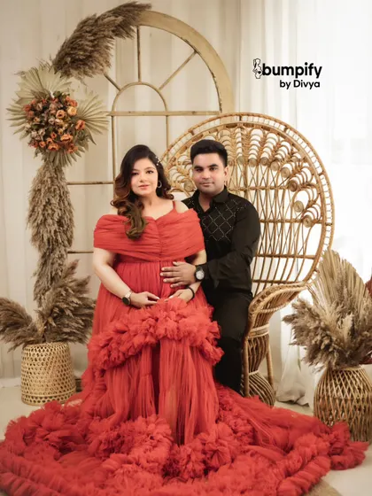 A portrait of regal elegance. The mom to be is seated on a peacock chair in a stunning red gown, creating a powerful and beautiful image in our boho studio.
