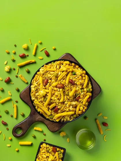 A top-down shot of Navratan Mixture for Sartaj Sweets & Namkeen. The vibrant green background and scattered ingredients create a dynamic, eye-catching image designed for modern snack packaging and e-commerce listings.