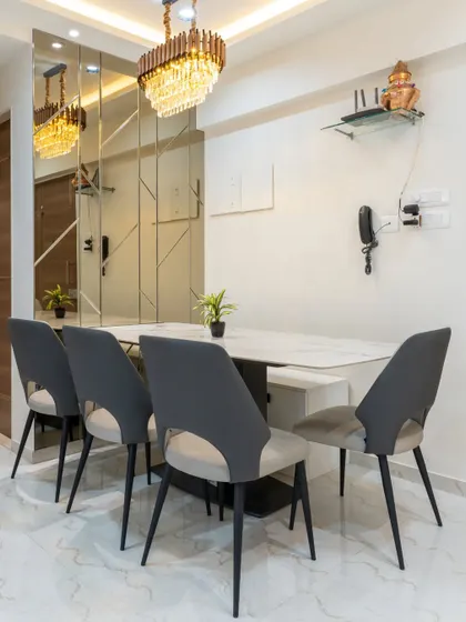 A glamorous dining space featuring a mirrored wall that visually doubles the room's size. The crystal chandelier and modern chairs add to the luxurious feel.