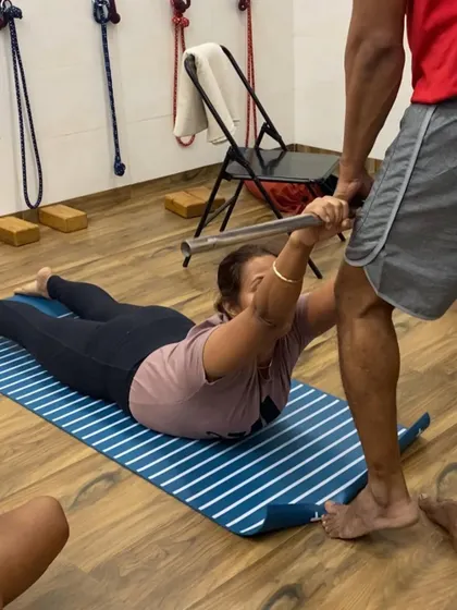I am assisting a student in Salabhasana (Locust Pose) using a metal rod. This prop helps the student to lift the chest and engage the back muscles correctly.
