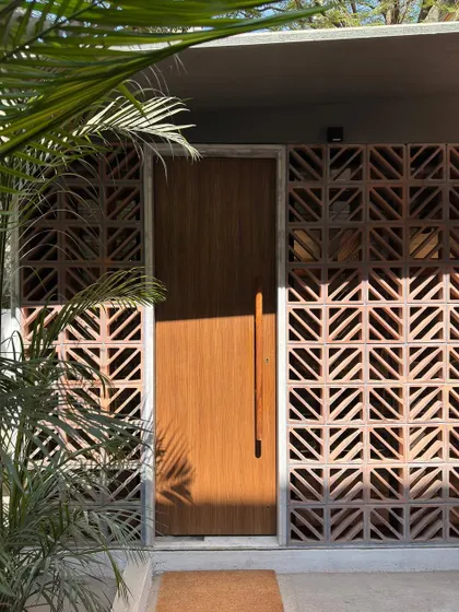 A close-up of the studio extension's entrance, where the warm wood of the door contrasts with the earthy terracotta jali. Lush green plants complete the picture, connecting the space to nature.