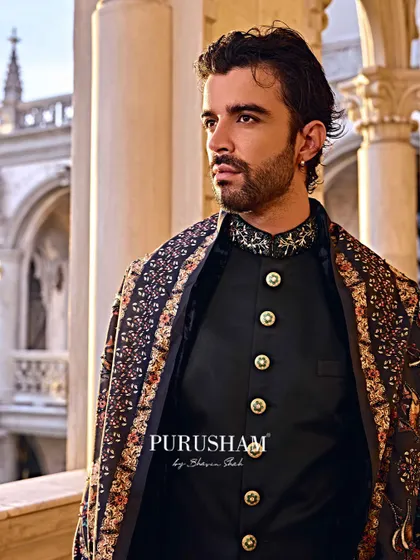 A close-up on the details. The embellished collar and custom buttons of this black bandhgala are set against the rich pattern of the shawl, creating a look of pure sovereignty.
