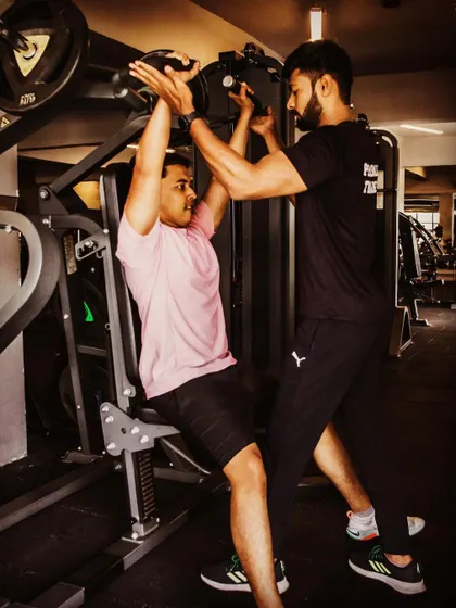 My role as a coach is to guide and push you safely. Here, I'm spotting a client during a shoulder press, ensuring correct form and providing the support needed to maximize the lift and prevent injury.