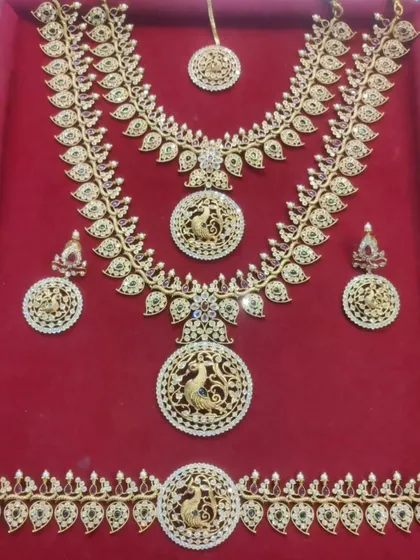 A beautiful peacock-motif bridal set laid out on a red velvet tray. This set includes a choker, haram, vaddanam, and matching earrings.