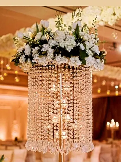 A luxurious centerpiece combining a tall crystal stand with a lush arrangement of white flowers, perfect for adding glamour to wedding reception tables.
