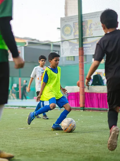 A young player in a bright bib navigates a practice game, showcasing his focus and control of the ball.