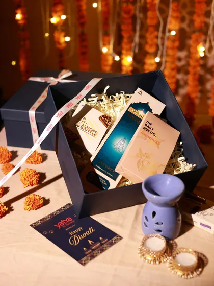An open view of a corporate gift box for Yatra, containing a diffuser, snacks, and other relaxing treats for a thoughtful Diwali present.