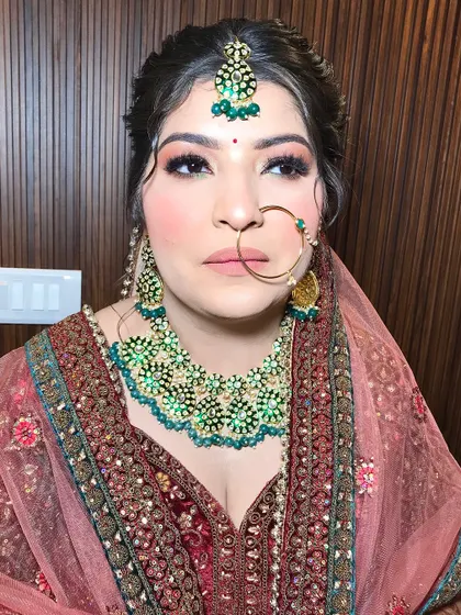 A close-up of Shanu's makeup, showing the soft smokey eye and nude pink lip that complements her heavy jewelry.