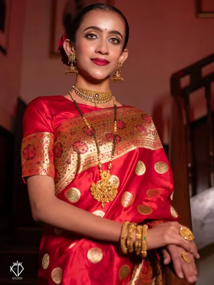 An indoor portrait using dramatic lighting to highlight the richness of the red saree and gold jewelry.