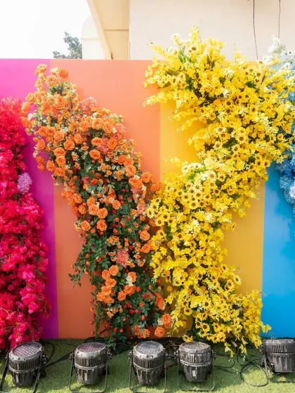 A vibrant photo wall made of colorful panels and cascading flowers in shades of orange and yellow, creating a perfect backdrop for guests' pictures.