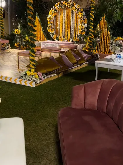 A wide view of an outdoor Haldi event, showing the main stage with marigold decorations and comfortable, modern seating arrangements for guests on the lawn.
