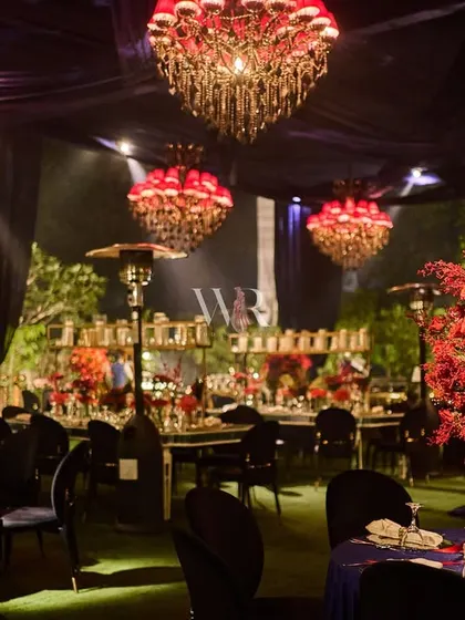 A beautiful overview of the red and blue themed dining area. The tables are covered in deep blue velvet, providing a rich base for the vibrant red floral centerpieces and the glow of the red chandeliers.