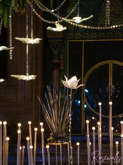 A closer look at the intricate lighting details. Here, illuminated lotus flowers and hanging crystal birds create a whimsical and luxurious feel against the dark, ornate doors of the venue.