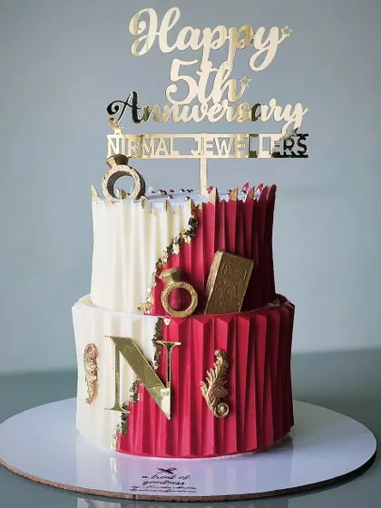 This two-tiered cake was for a corporate anniversary, featuring the company's initial and an origami-style texture. The red, white, and gold color scheme is bold and celebratory.