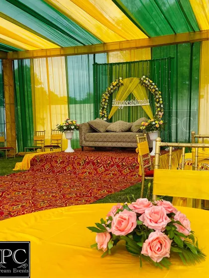 A wider view of the outdoor Mehndi setup, showing the tented area with green and yellow drapes and guest seating arrangements.