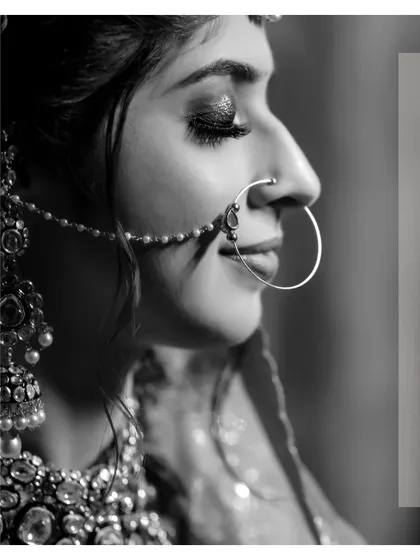 A striking black and white profile shot of the bride. The play of light and shadow beautifully highlights her features, especially her elegant nath (nose ring).