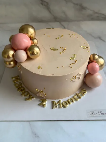 A simple and sweet cake for a two-month celebration, decorated with pink and gold spheres and delicate gold leaf.